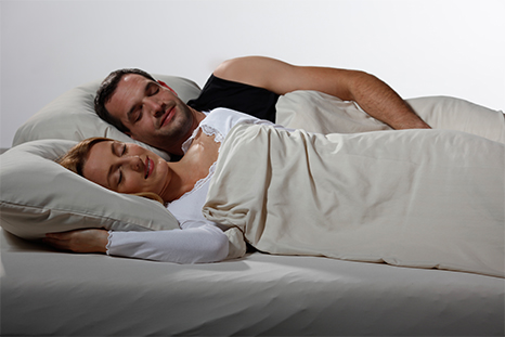 Mann trägt die Nachtwächter Schlafweste und liegt neben seiner Frau im Bett